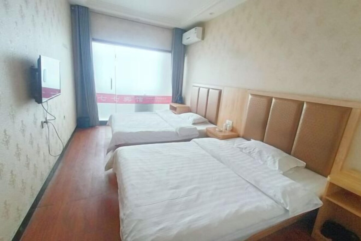 Habitación de hotel con dos camas, un televisor montado en la pared y una ventana con cortinas.