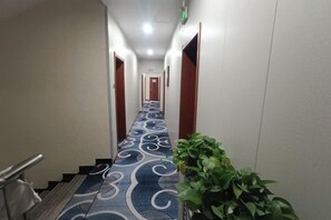Un pasillo de hotel con alfombra estampada, una escalera y una planta en maceta.