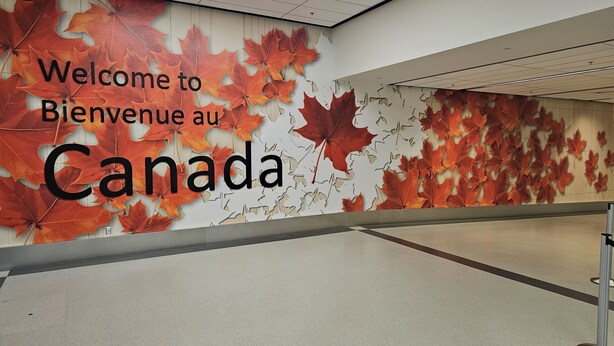 En væg med en velkomstskilt til Canada, prydet med efterårsblade og tekst på to sprog.
