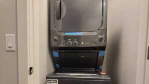 En kompakt vaske- og tørremaskine med kontrolpanel, placeret i en smal gang.