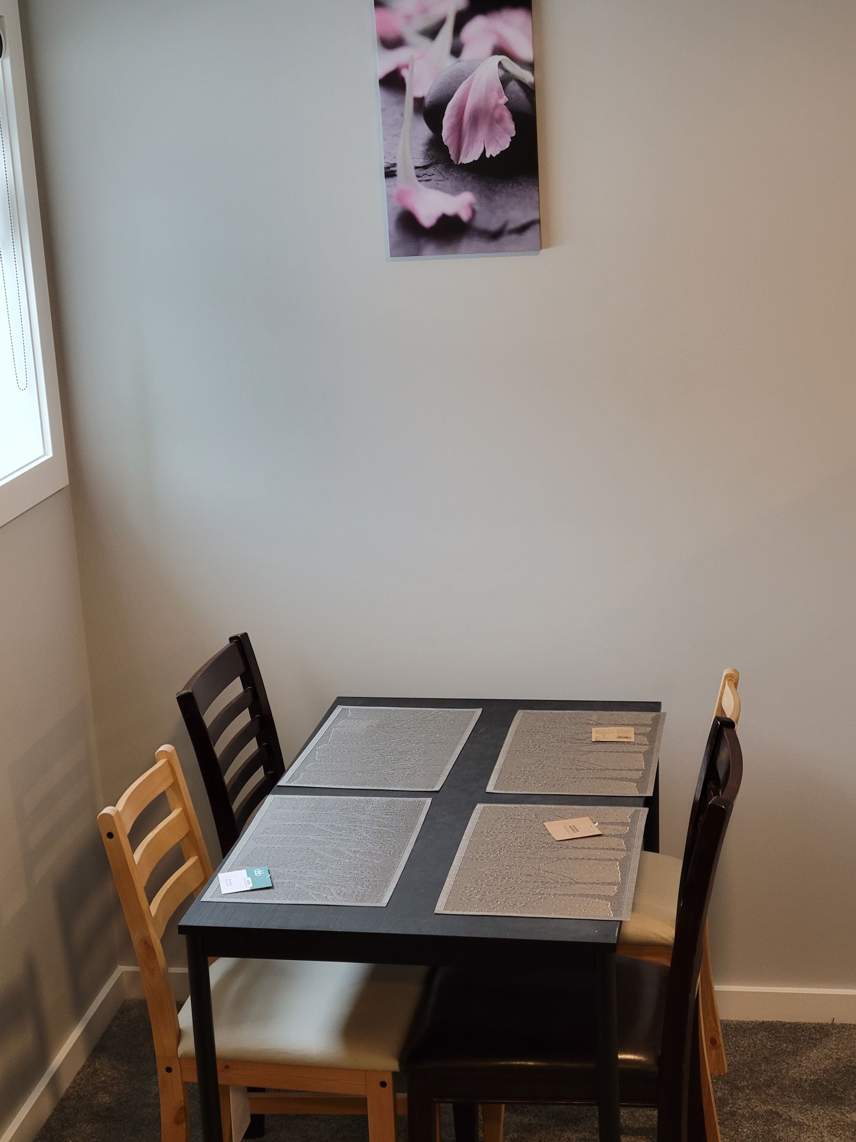 A dining table with four placemats, two wooden chairs, and a framed picture on the wall.