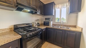 A kitchen with dark cabinets, a stove, oven, microwave, and a sink.