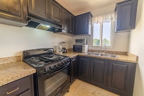 A kitchen with dark cabinets, a stove, oven, microwave, and a sink.