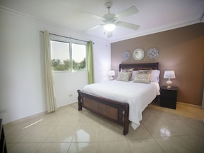 A bedroom with a bed, a ceiling fan, a nightstand, and a window with curtains.