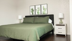 Een slaapkamer met een bed, twee nachtkastjes, en drie gepresenteerde cactusfoto’s aan de muur.