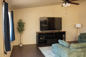 A living room with a flat-screen TV, a ceiling fan, a sofa, a floor lamp, and a potted plant. - 4BR Yuma, AZ Home - 8 Beds, Free Tesla Charger, Near MCAS Yuma & Foothills (Yuma)