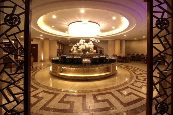 A hotel lobby with a central round bar, a chandelier, and a patterned floor.