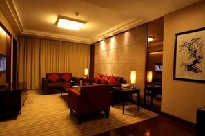 Une chambre d’hôtel avec un canapé, des fauteuils, une table basse, un téléviseur et un tableau au mur.