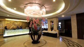 A lobby with a reception desk, a large decorative vase with flowers, and a modern chandelier. - Tashan Hotel Pujiang (Pujiang)