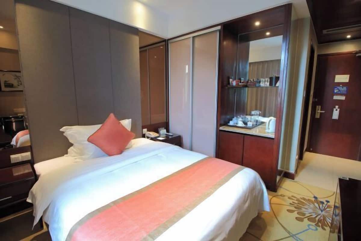 Une chambre d’hôtel avec un grand lit, une table de chevet, un bureau avec un miroir et une armoire.