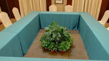A conference room with a table covered in a blue tablecloth, surrounded by chairs, and a potted plant with red flowers in the center.