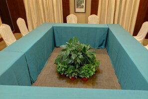 A conference room with a table covered in a blue tablecloth, surrounded by chairs, and a potted plant with red flowers in the center. - Tashan Hotel Pujiang (Pujiang)