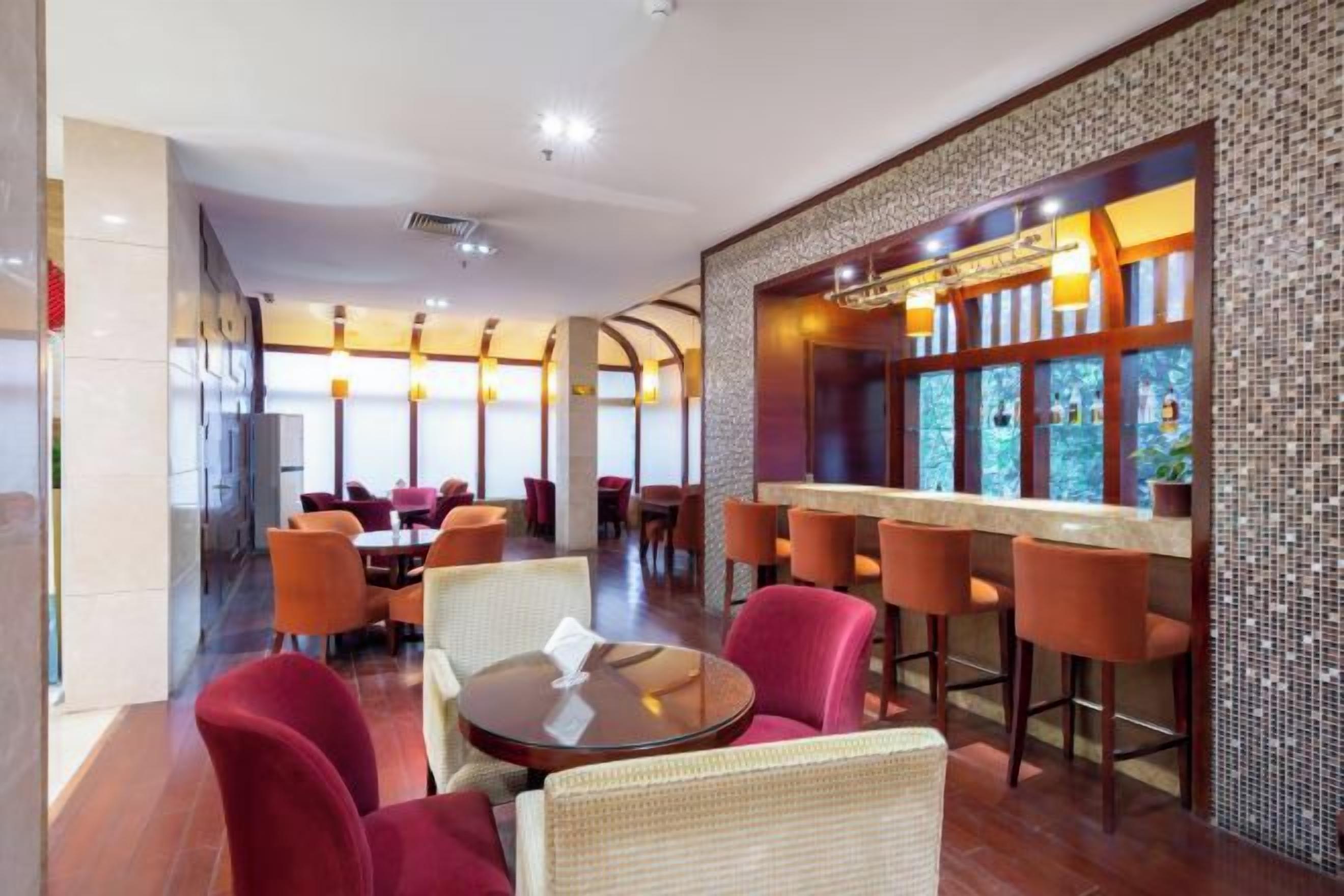 A restaurant with round tables and red chairs, a bar area with stools, and a tiled wall with a decorative pattern.
