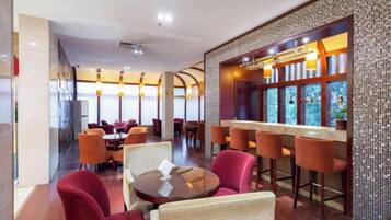 A restaurant with round tables and red chairs, a bar area with stools, and a tiled wall with a decorative pattern.