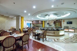 Un comedor de hotel con mesas redondas, sillas, una fuente decorativa en el centro y un televisor montado en la pared.
