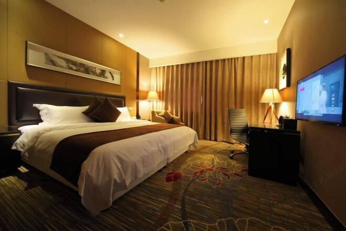 Une chambre d’hôtel avec un grand lit, deux lampes de chevet, un téléviseur à écran plat et une moquette à motifs floraux.