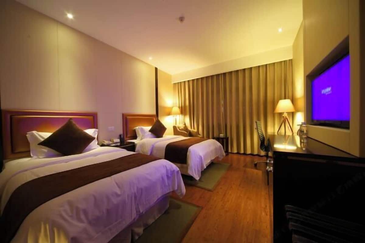 Une chambre d’hôtel avec deux lits, une télévision, un bureau et un rideau.