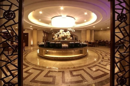 A lobby with a circular reception desk, a chandelier, and a patterned floor.. Tashan Hotel Pujiang