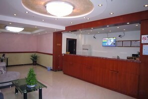 A hotel reception area with a wooden reception desk, a television screen, and a seating area with a plant. - Xiangxiu Hostel (Shanghai)