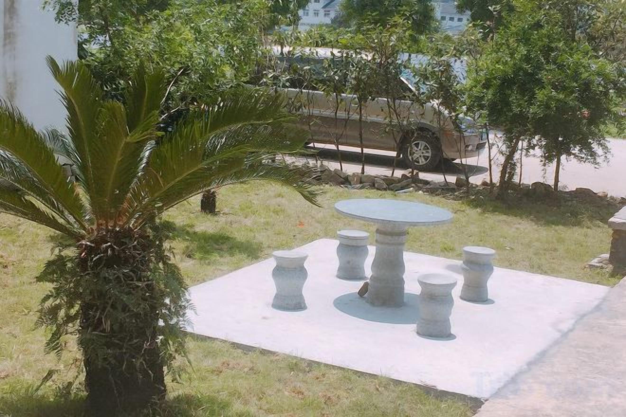 Un patio con una mesa redonda y cuatro sillas, rodeado de césped y una palmera.