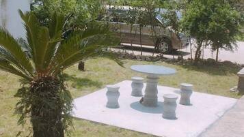 Un patio con una mesa redonda y cuatro sillas, rodeado de césped y una palmera.