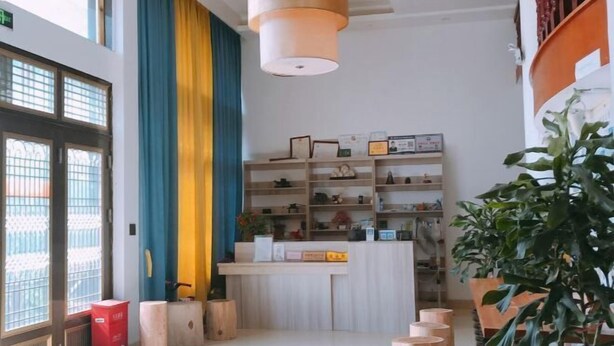A modern interior with a reception desk, wooden stools, and a large potted plant. - Xinyue Inn (Yueqing)
