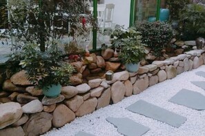 Un jardín con muro de piedra, plantas en macetas y piedras para caminar.