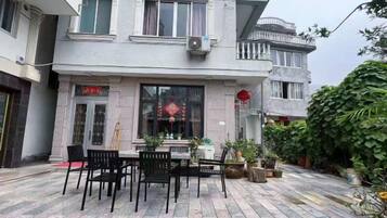 A courtyard with a dining table and chairs, surrounded by potted plants and a building with a traditional design.