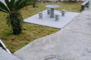 A concrete patio with a round table and six chairs, surrounded by grass and a palm tree. - Xinyue Inn (Yueqing)