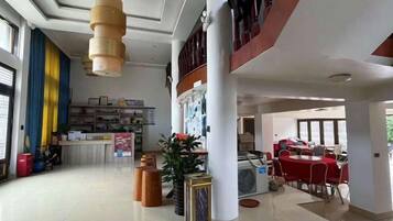Un vestíbulo espacioso con mostrador de recepción, zona de comedor con mesas rojas y una escalera que sube a un nivel superior.