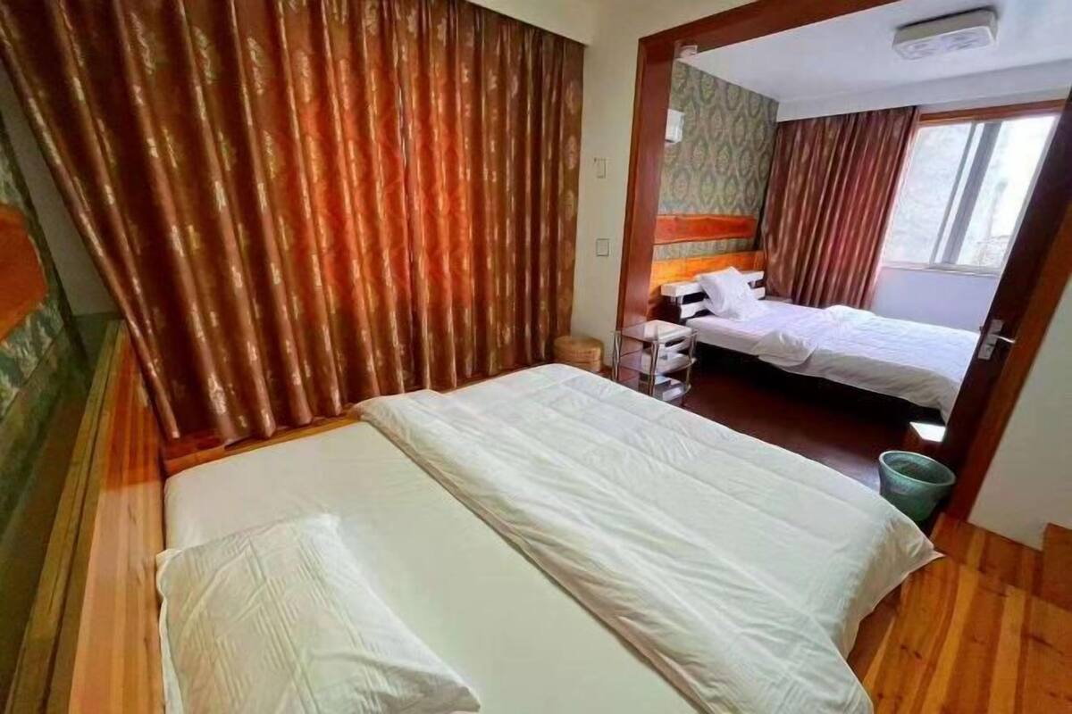 A room with two beds, a wooden floor, a window, and a curtain.