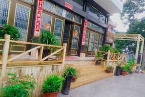 A traditional building with a wooden entrance, potted plants, and red banners. - Xinyue Inn (Yueqing)