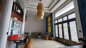 A spacious lobby with a high ceiling, a central wooden table, seating area, and large windows with metal bars. - Xinyue Inn (Yueqing)
