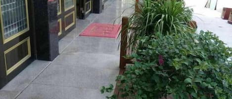 A corridor with a tiled floor, a wooden planter with green plants, and a red mat on the ground.