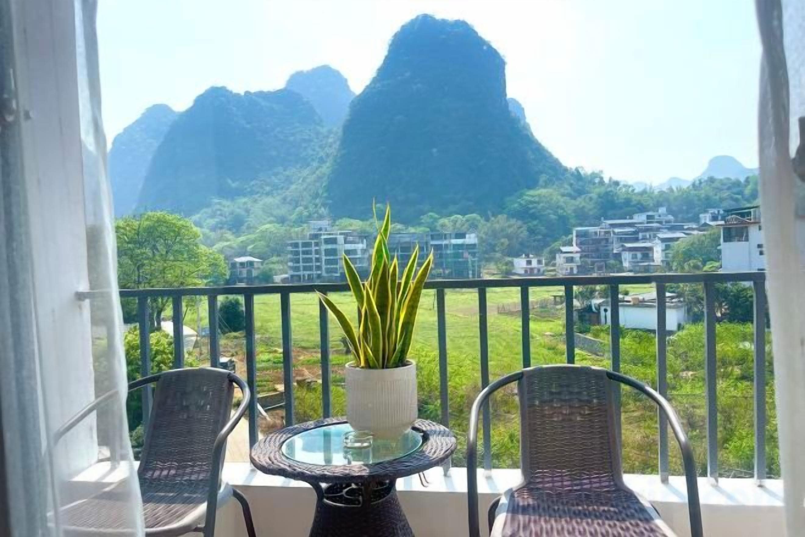 Een balkon met een tafel en stoelen, met uitzicht op een bergachtig landschap met gebouwen in de verte.