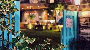 A nighttime view of a courtyard with a blue gate, a sign, and a well-lit interior space.