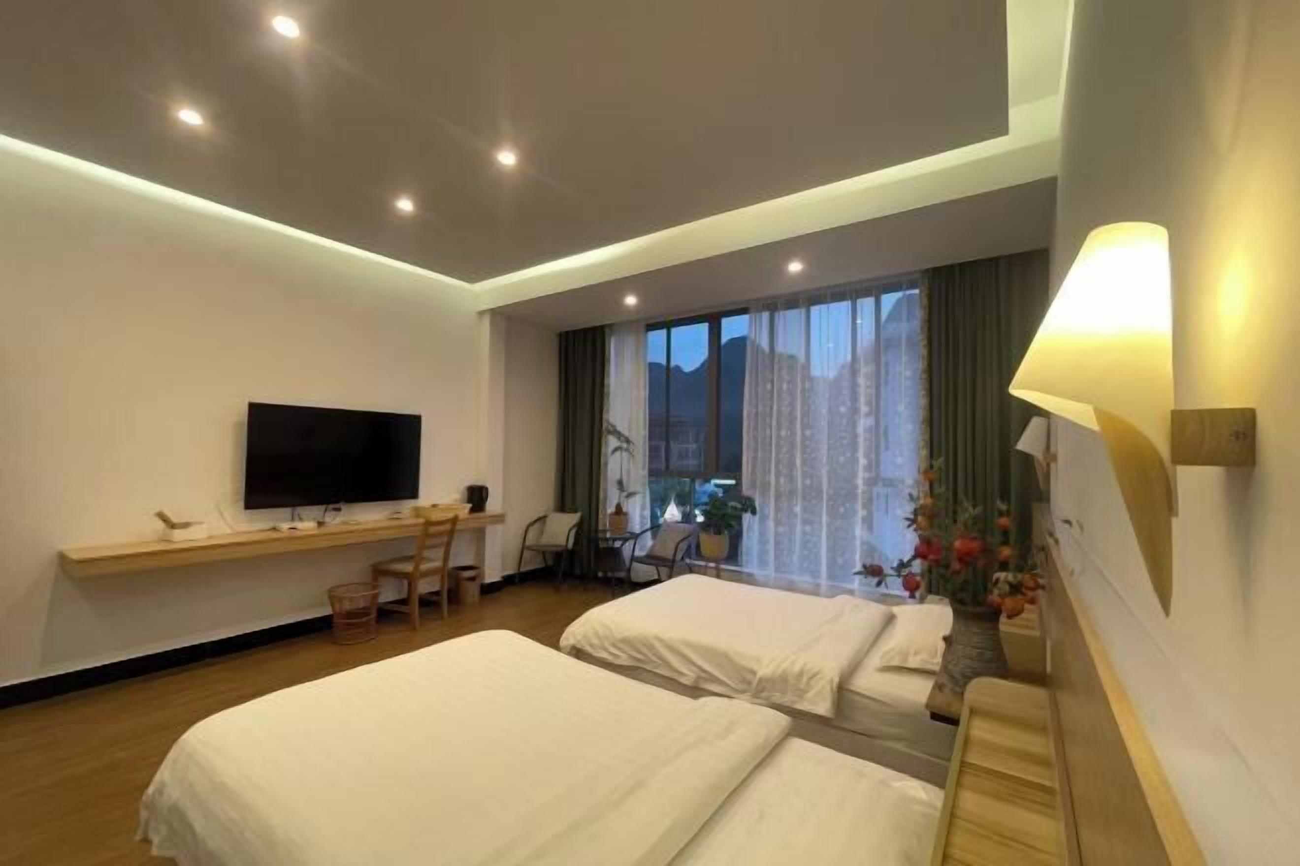 Habitación de hotel con dos camas, un escritorio, televisor y un ventanal con cortinas.