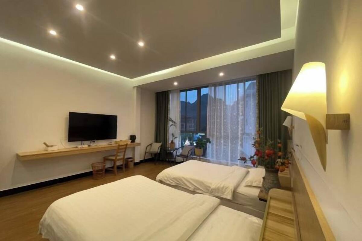 Une chambre d’hôtel avec deux lits, un bureau, une télévision et une grande fenêtre avec des rideaux.