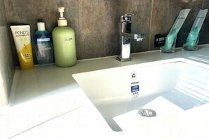 A bathroom with a white sink, a mirror, and toiletries including a bottle of Pond's lotion, a blue bottle, and a green bottle.