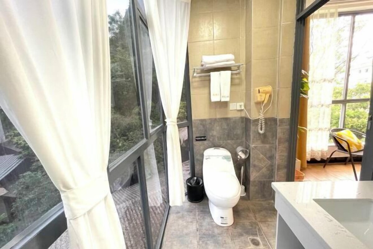 A modern bathroom with a toilet, a sink, and a shower area. There is a window with curtains, a towel rack, and a telephone.