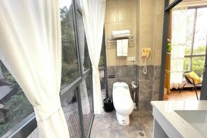 A modern bathroom with a toilet, a sink, and a shower area. There is a window with curtains, a towel rack, and a telephone.