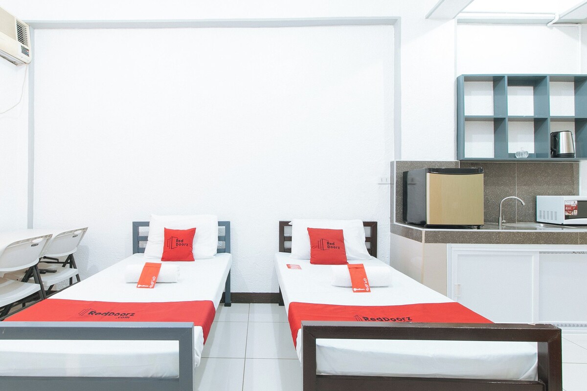 A twin room with two beds, a desk, a chair, a small kitchenette, and a window with curtains.