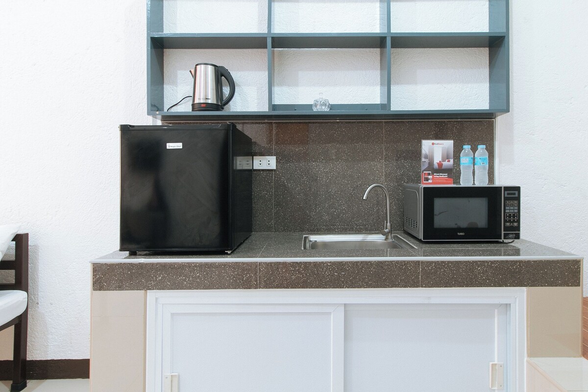 A compact kitchen with a refrigerator, microwave, sink, and a shelf above the countertop.