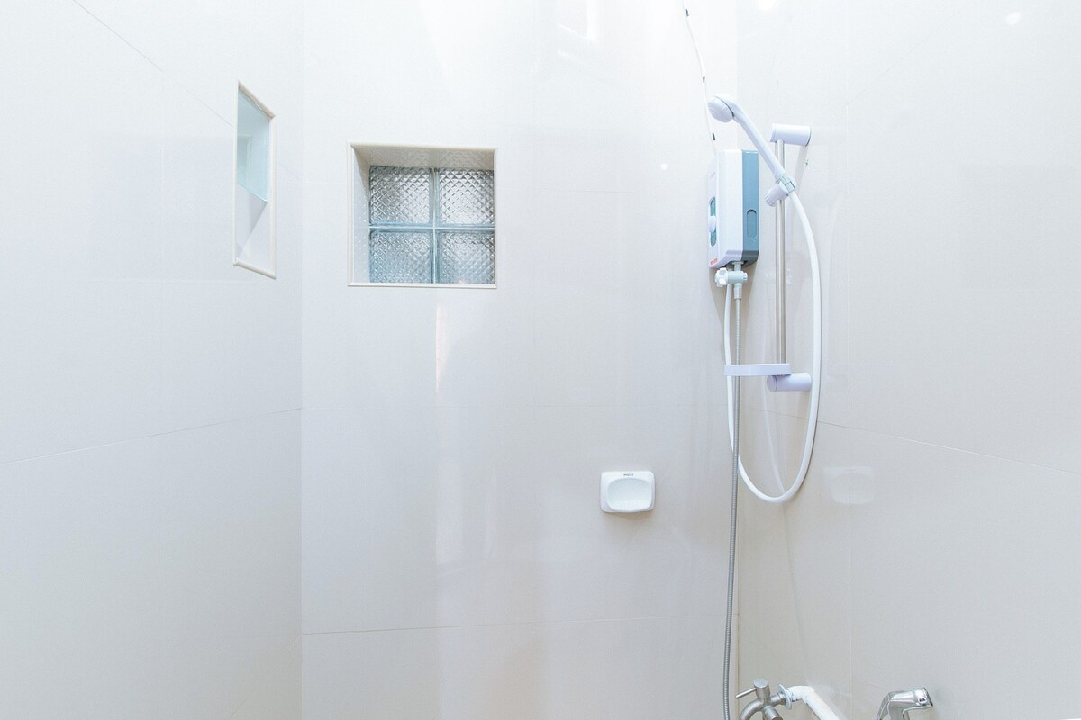 A white shower with a handheld showerhead and a wall-mounted faucet.