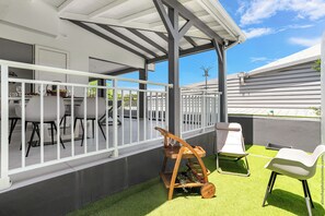 Une terrasse extérieure couverte, dotée d’une balustrade blanche, d’un porte-bouteilles en bois et d’une chaise blanche.