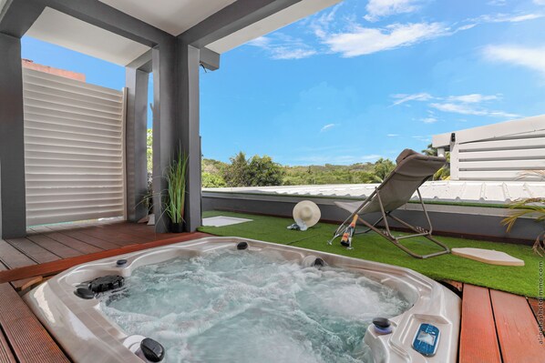 Un bain à remous avec une terrasse en bois, une chaise longue et une vue sur le paysage.