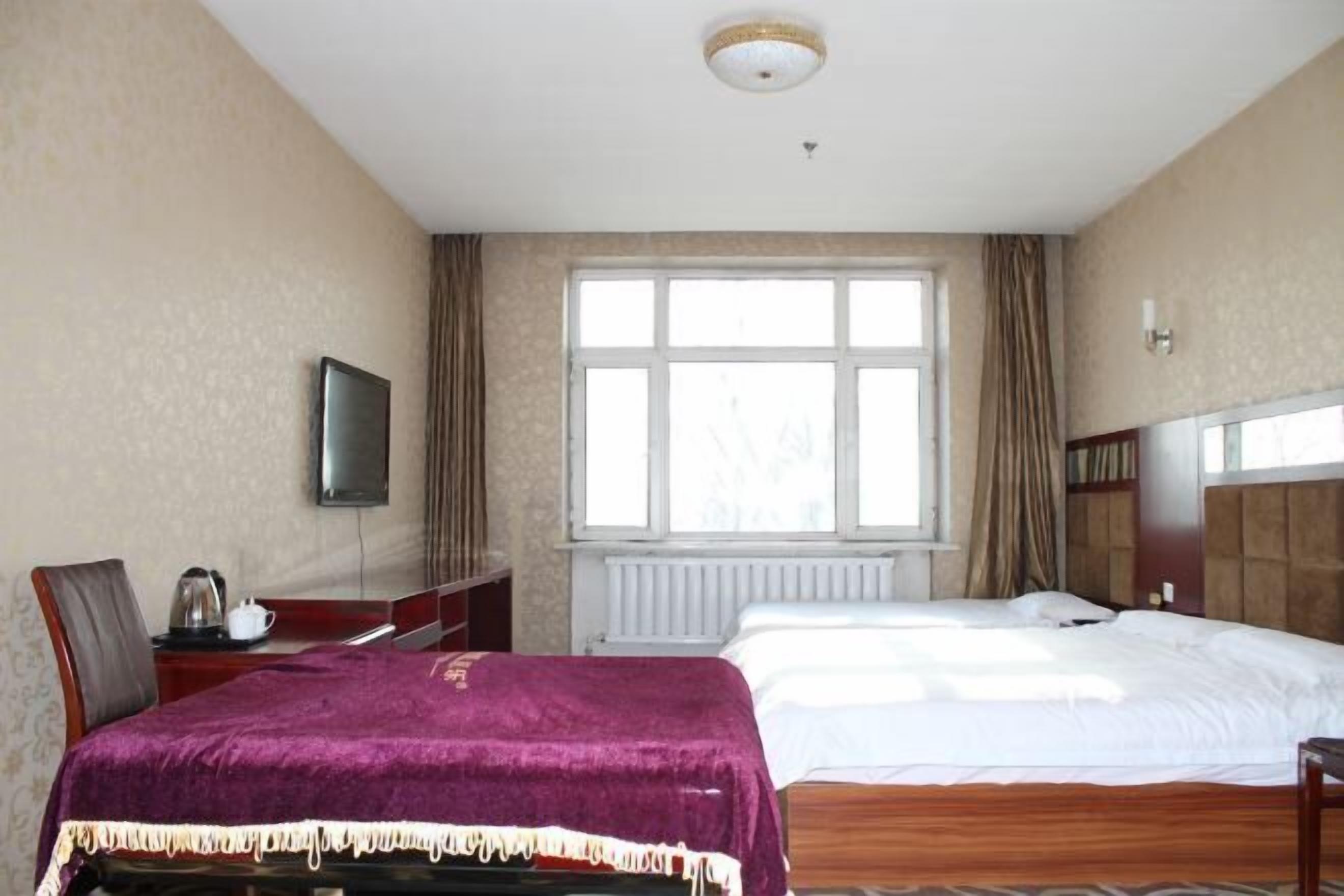 Een hotelkamer met twee bedden, een televisie, een bureau met een waterkoker en een raam met gordijnen.