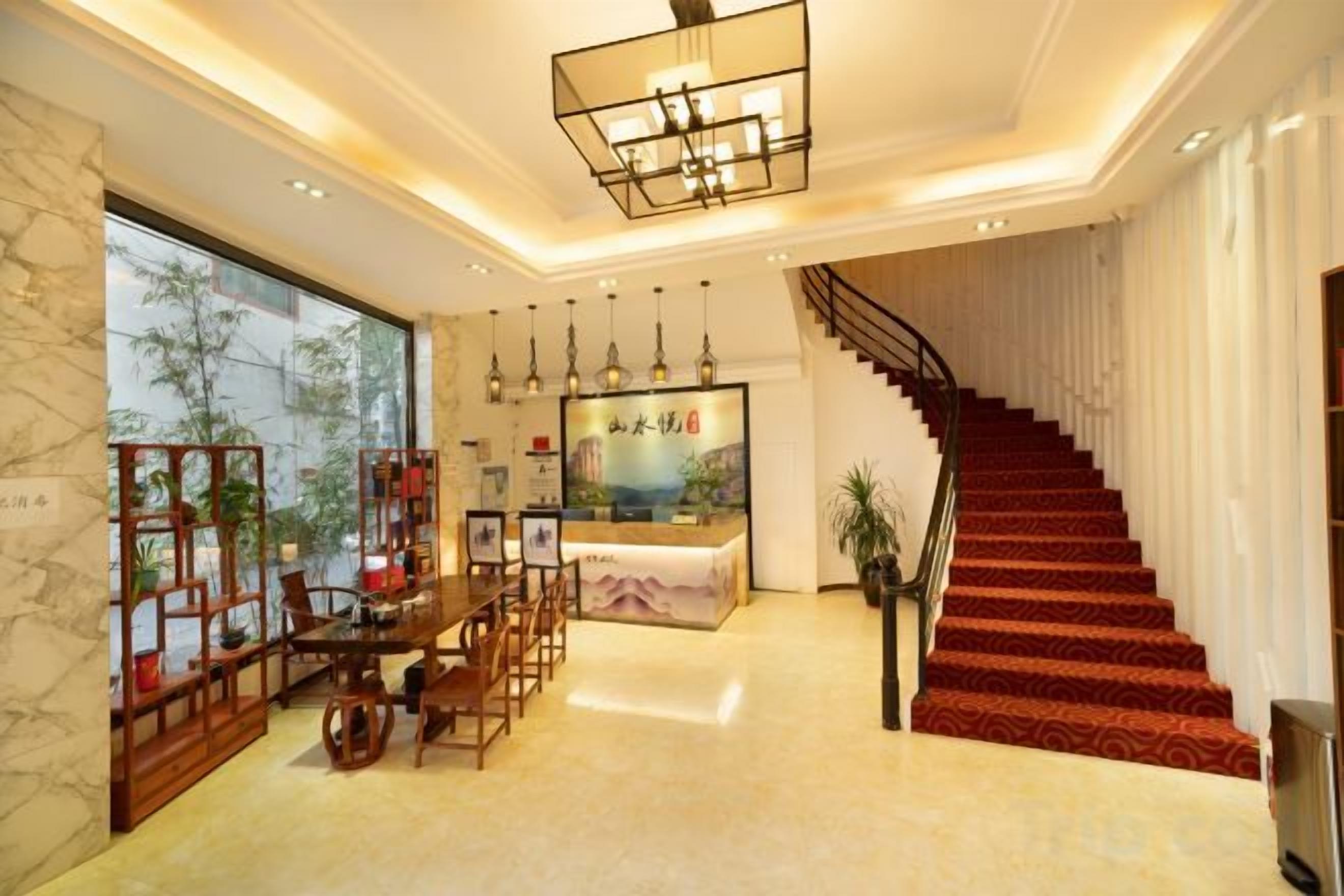 Eine Hotlellobby mit einer Rezeption, einer Treppe und einem Essbereich mit Stühlen und Tischen.