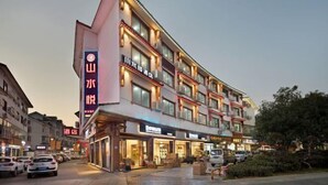 Et hotel med flere etager, et tydeligt skilt på venstre side, flere altaner og forskellige butikker i stueetagen.