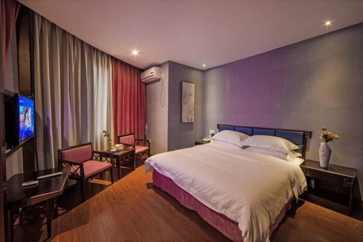 A hotel room with a bed, a desk, a chair, a TV, and an air conditioning unit.